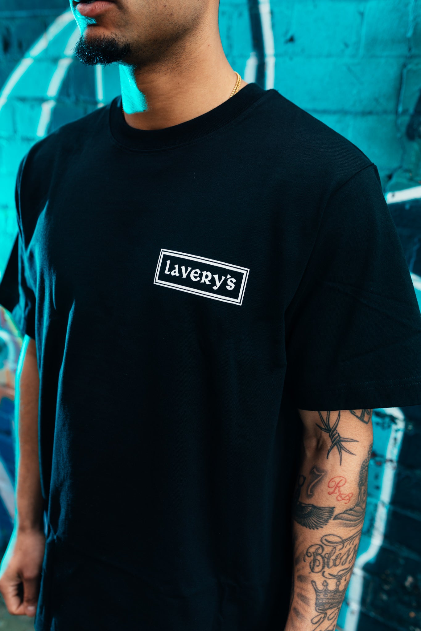 Person wearing a black t-shirt with 'Lavery's' logo against a blue graffiti wall.