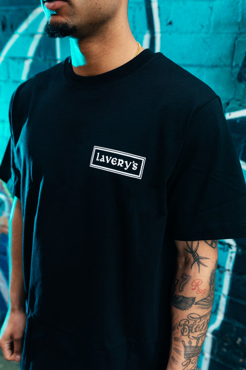 Person wearing a black t-shirt with 'Lavery's' logo against a blue graffiti wall.